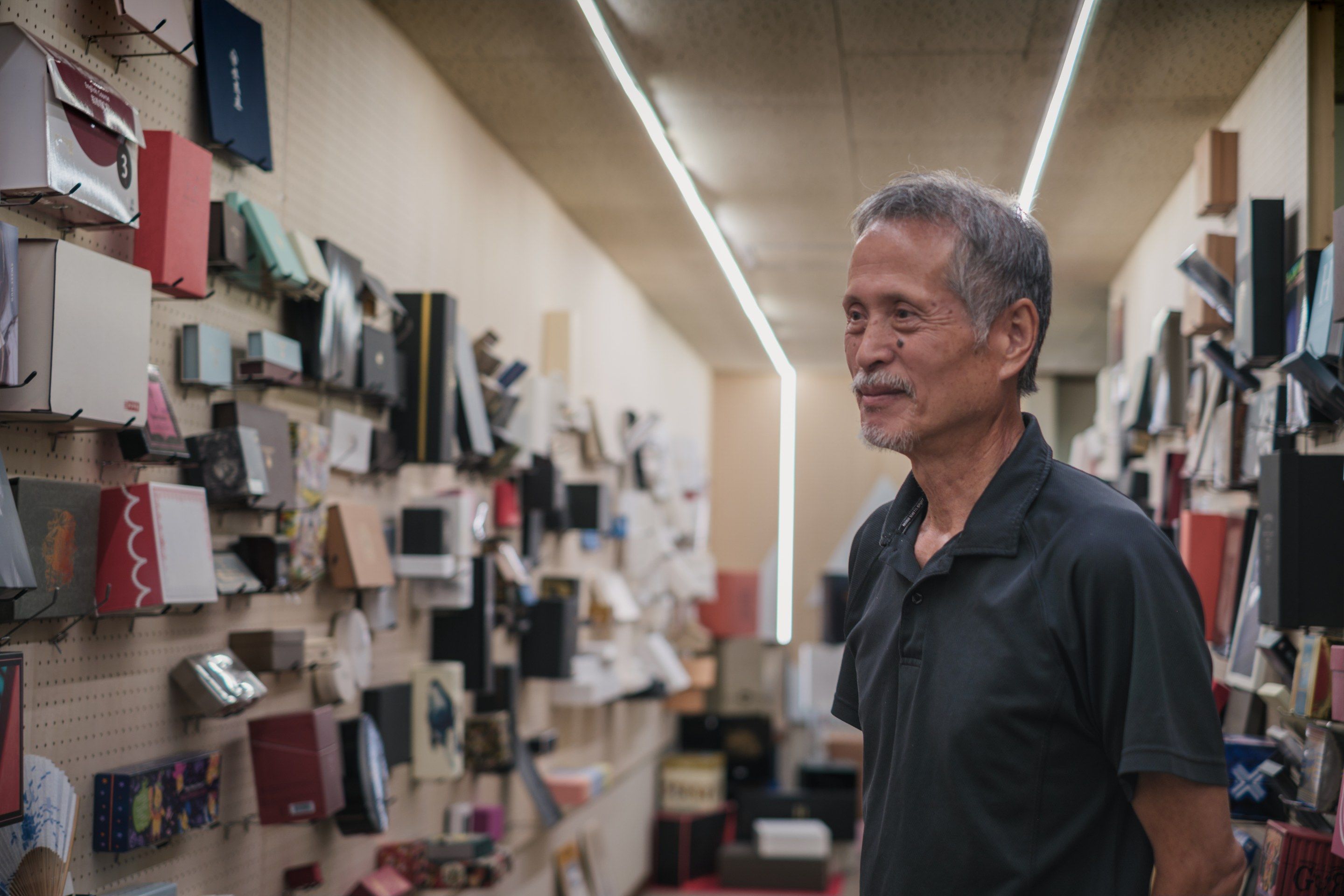 箱の見本が壁一面に掛かった通路で、右を向いてほほえむ赤池富士夫さん