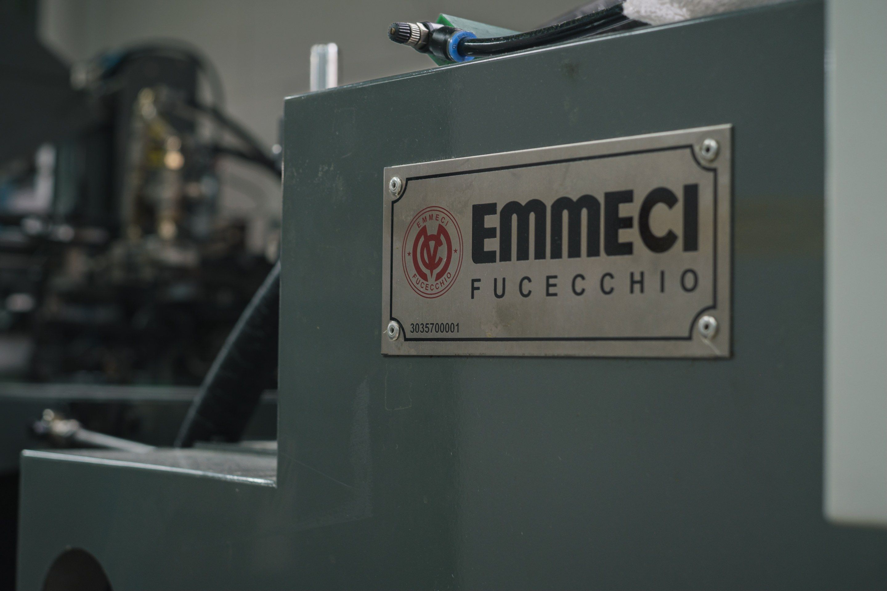 濃い緑色の機械の側面に付いた銀色の銘板。赤い印と「EMMECI FUCECCHIO」の字