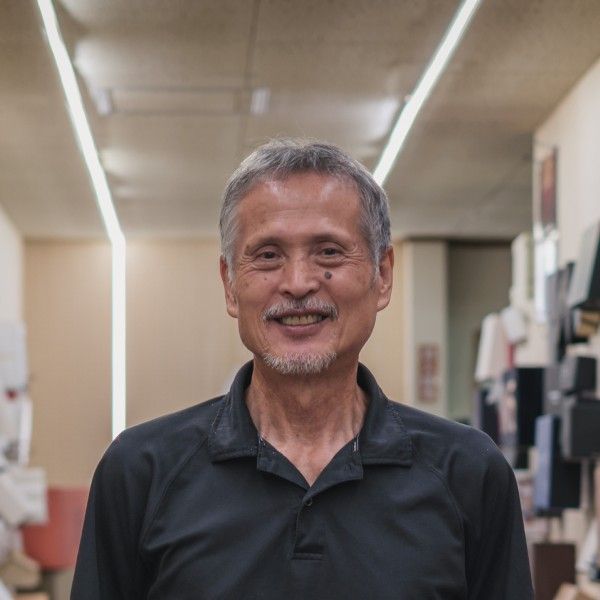 白髪まじりの短い髪に、あごひげのある赤池富士夫さんが、黒いポロシャツ姿で笑っている