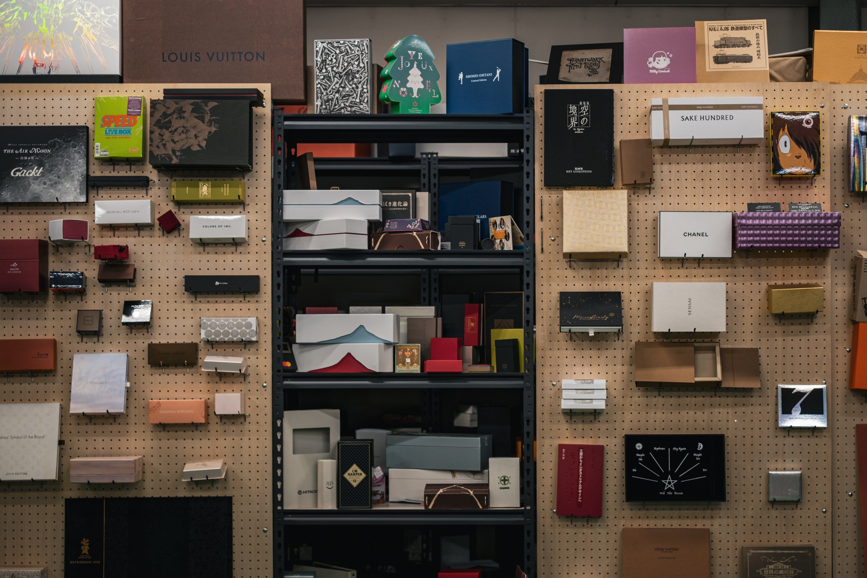 壁一面の穴開きの板と黒い棚に、箱の見本がぎっしり並ぶ。上のほうに「LOUIS VUITTON」と入った箱がある