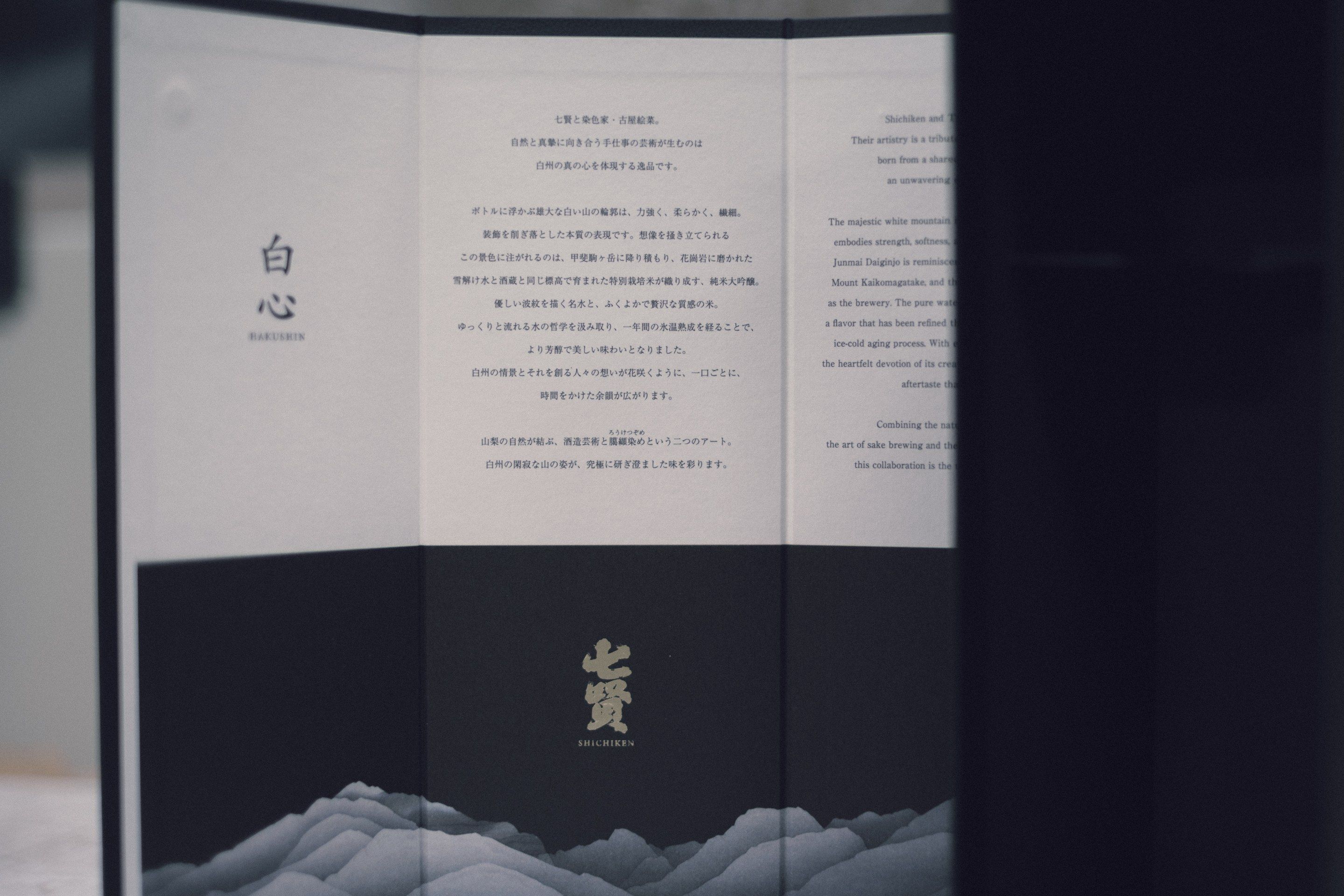 屏風のように三つに開いたパッケージ。左に「白心」の字、中央に日本語と英語の説明文、下半分は黒地に金の「七賢」の字と、灰色の山並みの絵